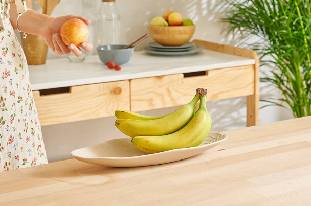 Γυναίκα προσφέρει μπανάνες στην κουζίνα, ξύλινο τραπέζι. - Φωτογραφία, εικόνα