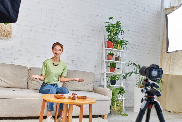 smiling woman presenting vegetarian meal during video blog on plant-based diets in green living room - Foto, Imagem