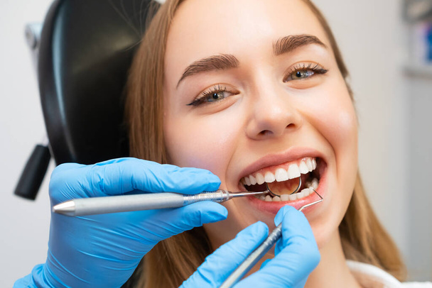 Pacjentka siedząca na krześle w gabinecie stomatologicznym. Lekarz sprawdza przednie zęby za pomocą przyrządów do sprawdzania wytrzymałości zębów - Zdjęcie, obraz