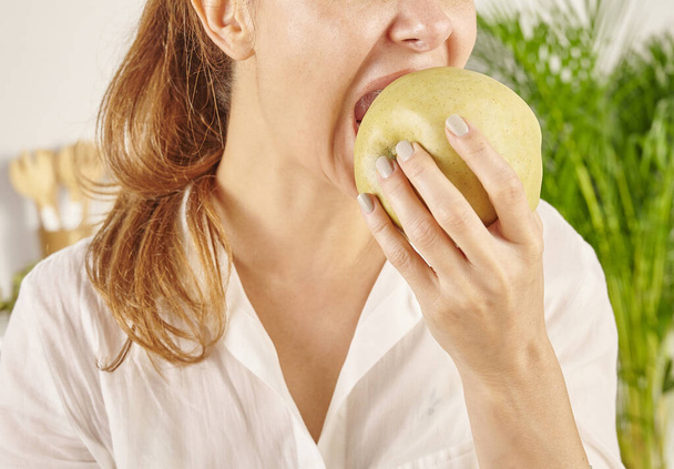Woman eating apple, close-up, mouth and hand. Kitchen background style. - Photo, Image