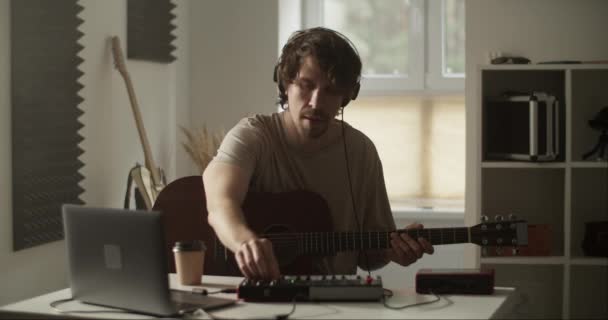 Міленіал гітарист в навушниках встановлює мікшер під час створення музики та відтворення акустичної гітари в домашній студії - Кадри, відео