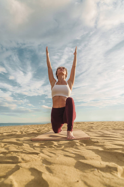 Plan vertical d'une jeune femme de vingt ans exécutant la pose de yoga Sun Salutation face à l'avant sur la plage - Photo, image