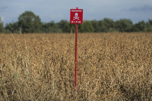 Um sinal de alerta com a inscrição em ucraniano DANGEROUS MINE é instalado em um campo de agricultores no norte da Ucrânia. Foto de alta qualidade - Foto, Imagem