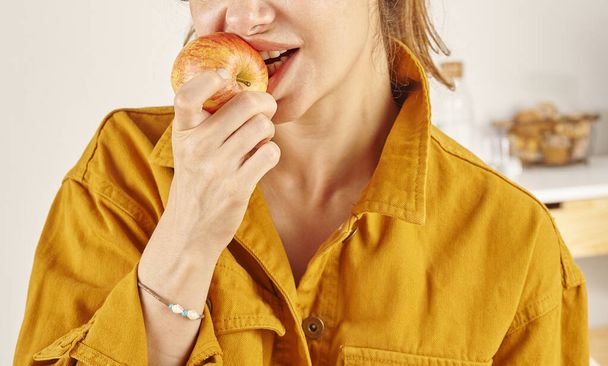 Donna che mangia mela, primo piano, mano e bocca. Cucina sfondo. - Foto, immagini