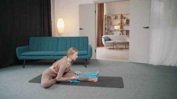 Een jonge vrouw die sport in een lichte huiskamer. Gebruikt sportbeha 's voor stretching - Video