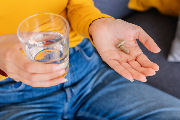 Feche as mãos jovem mulher segurando cápsula pílula alimentos complementares e copo de água. Vitaminas, comprimidos e comprimidos. Conceito de cuidados de saúde e pessoas. - Foto, Imagem