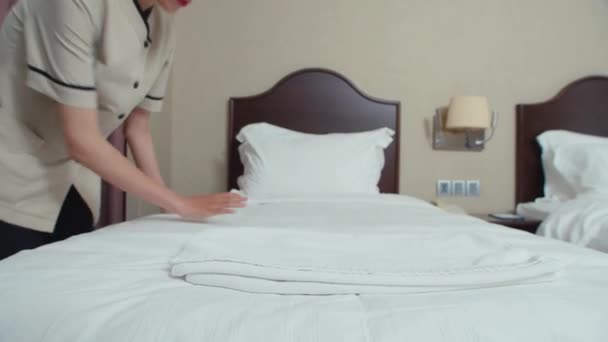 Mediana largo tiro de joven mucama cambio de ropa blanca en la cama en la habitación para los clientes - Imágenes, Vídeo