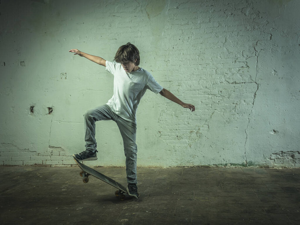 Мальчик тренируется на скейтборде. Фон имеет промышленную атмосферу с белой окрашенной кирпичной стеной. - Фото, изображение