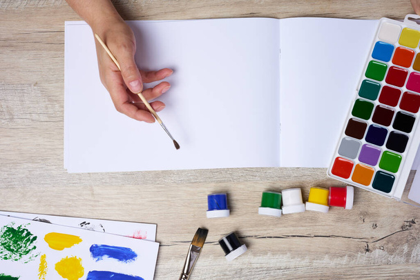 Set Aquarellfarben, Pinsel und Papier mit verschiedenen Strichen und Farben. Weibliche Hände, die einen Pinsel halten - Foto, Bild