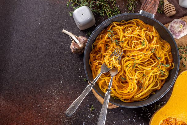 Домашняя осенняя тыквенная паста-спагетти, веганская средиземноморская, американская вегетарианская потепление еда с сырным тыквенным соусом, чеснок и тимьян, темно-бетонный фон - Фото, изображение