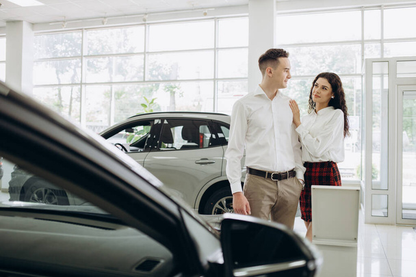 Visitando concesionario de coches. Hermosa pareja está sosteniendo una llave de su nuevo coche, mirando a la cámara y sonriendo. Foto de alta calidad - Foto, imagen