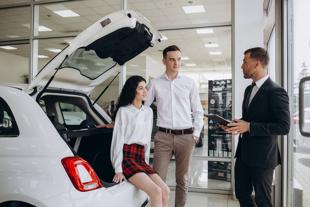 Genç çift başarılı araba satın alma sonra satış temsilcisi ile tokalaşırken.  - Fotoğraf, Görsel