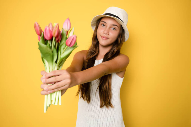 Sarı arka planda izole edilmiş çiçekleri tutan güzel kız çocuğunun portresi. - Fotoğraf, Görsel
