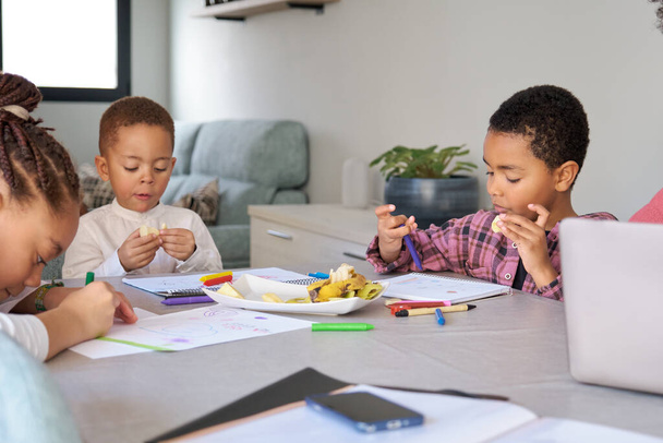 Троє дітей перекушують під час малювання або домашнього завдання вдома. - Фото, зображення