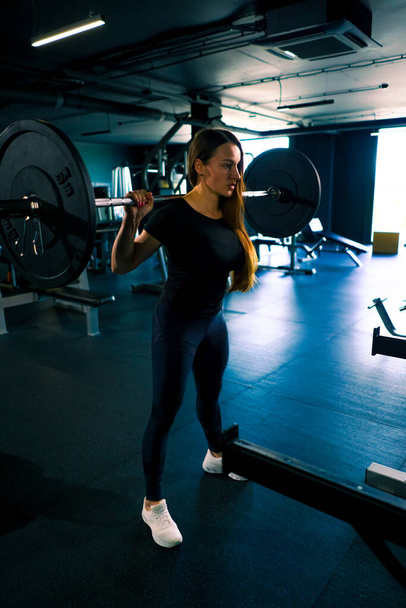geconcentreerde fitness vrouw doet zware schouder pers oefening met lange halter sportschool training spiergroep - Foto, afbeelding