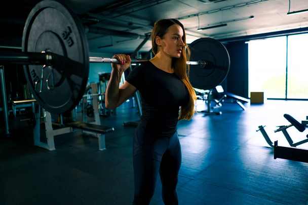 mujer de fitness concentrado haciendo ejercicio de presión de hombro pesado con barra gimnasio entrenamiento grupo muscular - Foto, Imagen