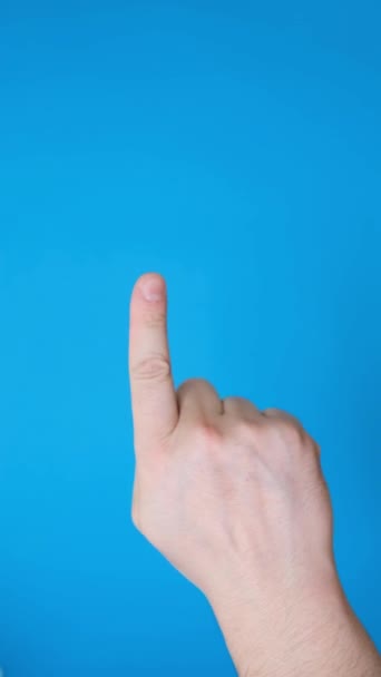 Mano maschile punta un dito di lato, facendo un gesto della mano, isolato su uno sfondo blu. Gesto della mano isolato su sfondo blu. Video verticale - Filmati, video