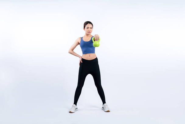 孤立した背景で運動を持ち上げるケトルベル体重をしている活発な女性. ボディワークアウトルーチンとしての若い運動アジアの女性の強さと耐久トレーニングセッション. - 写真・画像