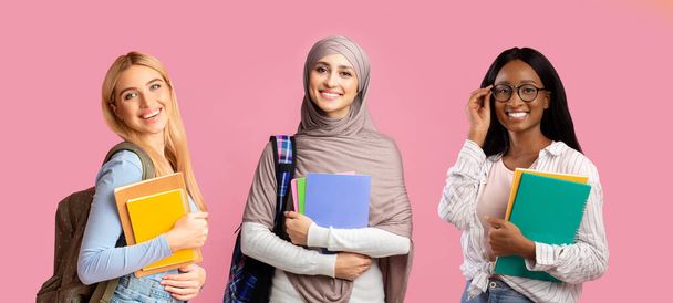 Tre studentesse multietniche che trasportano zaini e cartelle di lavoro in posa su sfondo rosa, gruppo di giovani donne allegre che sorridono alla macchina fotografica mentre si trovano su uno sfondo colorato, collage - Foto, immagini