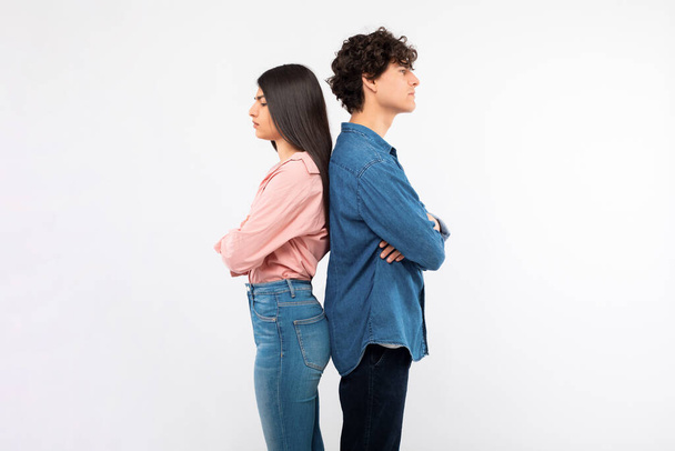 Offence. Frustrated young couple standing back to back sulking and not talking, posing on white studio background, crossing arms. Side view of girlfriend and boyfriend having issue in relationship - Photo, Image