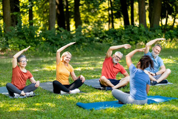 Sporty mature people doing stretching exercises during group lesson with instructor outdoors, happy senior men and women exercising outside, enjoying active lifestyle on retirement, free space - Photo, Image