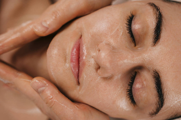 Detailní portrét mladé ženy s pěnovou masáží obličeje v lázeňském salonu. Masážní procedura. Tváří v tvář. Léčba obličeje. - Fotografie, Obrázek