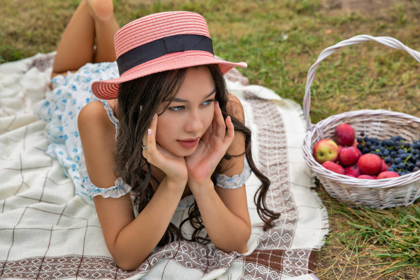 Beautiful young brunette caucasian woman wearing hat lying in the orchard garden. - Photo, Image