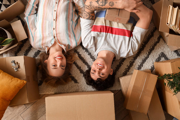 Young couple with moving boxes lying on carpet, top view - Photo, Image