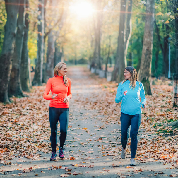 Γυναίκες τρέχουν στο δημόσιο πάρκο το φθινόπωρο. - Φωτογραφία, εικόνα