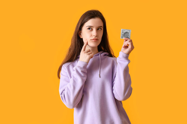 Nachdenklich junge Frau mit Kondom auf orangefarbenem Hintergrund - Foto, Bild