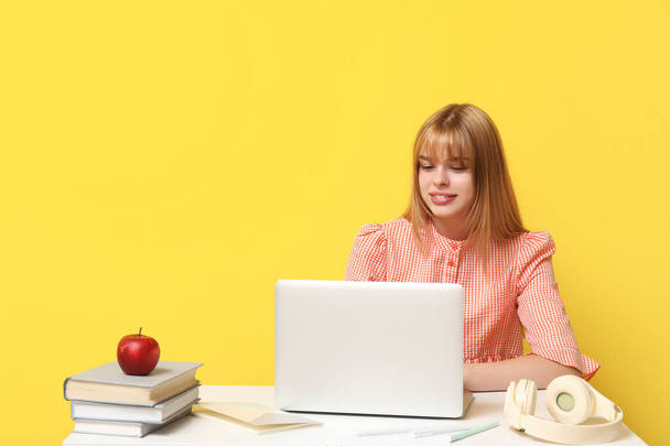 Estudante feminina com laptop fazendo lição de casa na mesa no fundo amarelo - Foto, Imagem
