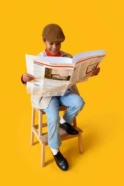 アフリカ系アメリカ人の少年が黄色い背景で新聞を読んでいる. - 写真・画像