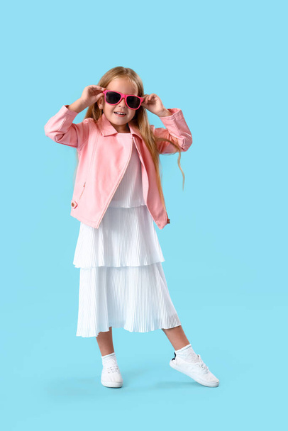 Cute little girl w okularach przeciwsłonecznych na niebieskim tle - Zdjęcie, obraz