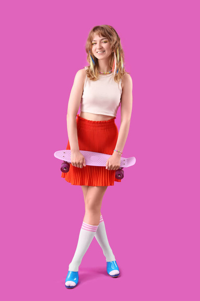 Молодая женщина со скейтбордом на фиолетовом фоне - Фото, изображение