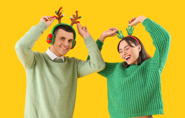 Happy beautiful young couple in Christmas reindeer horns on yellow background - Photo, Image