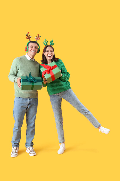 Happy young couple in Christmas reindeer horns with gift boxes on yellow background - Photo, Image
