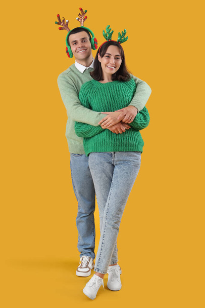 Boldog szép fiatal pár a karácsonyi rénszarvas szarvak sárga háttér - Fotó, kép