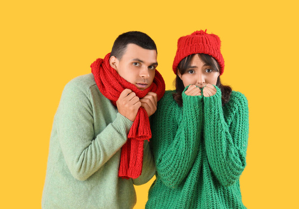 Jeune couple congelé en vêtements chauds sur fond jaune - Photo, image