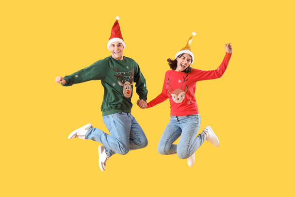 Schönes junges Paar in Weihnachtskleidung springt auf gelbem Hintergrund - Foto, Bild
