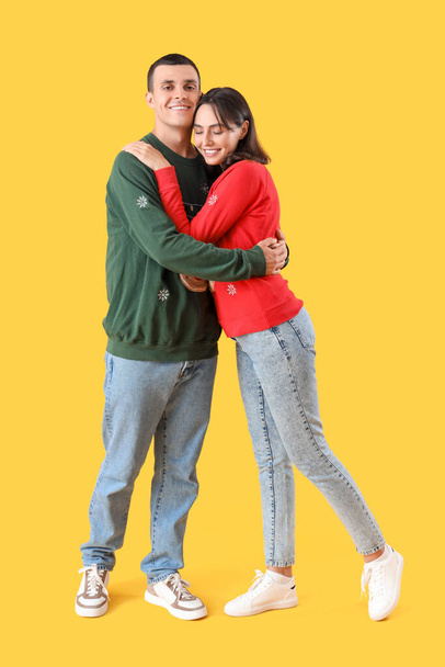 Красива молода пара в різдвяному одязі обіймається на жовтому тлі - Фото, зображення