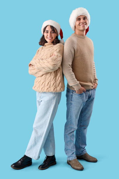Happy young couple in Santa hats on blue background - Photo, Image