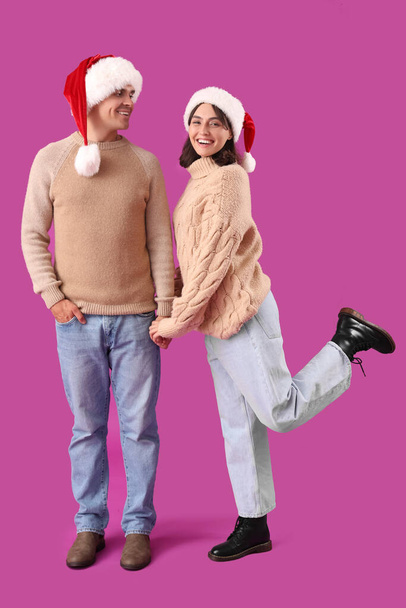 Feliz pareja joven en sombreros de Santa sobre fondo púrpura - Foto, imagen