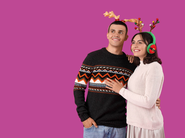 Feliz pareja joven en cuernos de renos de Navidad sobre fondo púrpura - Foto, imagen
