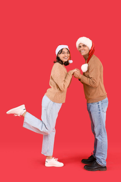 Kırmızı arka planda Noel Baba şapkalı mutlu çift - Fotoğraf, Görsel