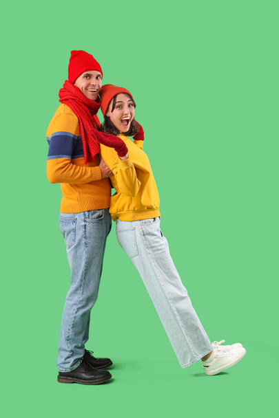 Happy young couple in warm clothes having fun on green background - Photo, Image