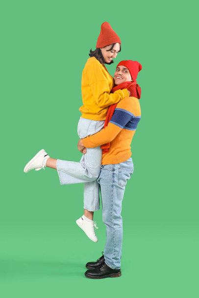 Happy young couple in warm clothes having fun on green background - Photo, Image