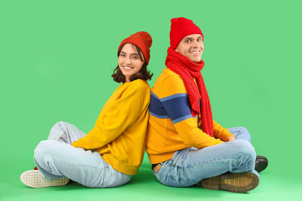 Happy young couple in warm clothes sitting on green background - Photo, Image