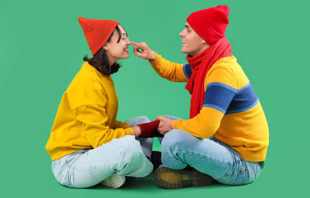 gelukkig jong paar in warme kleren zitten op groene achtergrond - Foto, afbeelding