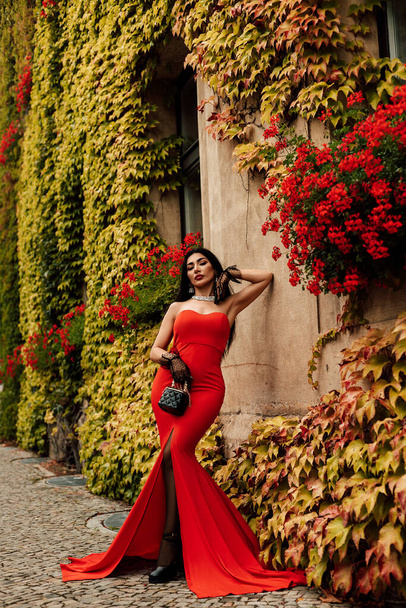 Жінка в червоній довгій сукні стоїть біля будівлі з квітами. Високоякісна фотографія - Фото, зображення