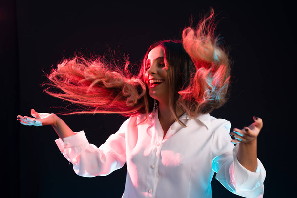 Beautiful, young attractive Caucasian woman wearing white clothing and throwing her hair forward. Isolated on black background. - Photo, Image